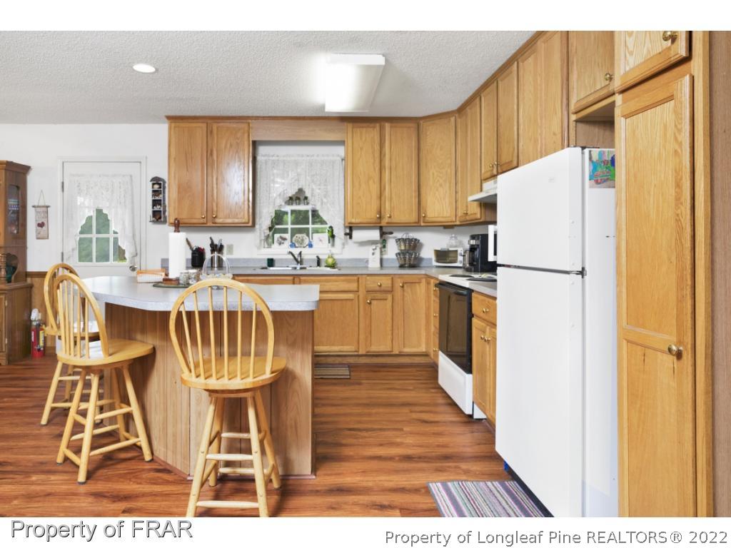 5253 Lobelia Road Vass, NC 28394 - Photo 13 of 28 a kitchen with granite countertop a refrigerator a stove a sink dishwasher and white cabinets with wooden floor