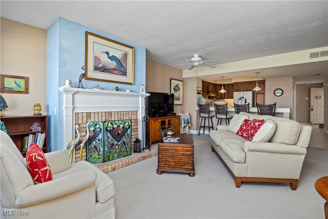 1507 Cleveland Road East, Unit 435 Huron, OH 44839 - Photo 7 of 37 Carpeted living room with ceiling fan, a fireplace, and a textured ceiling