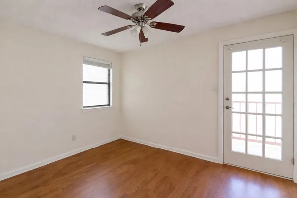 an empty room with wooden floor windows and fan