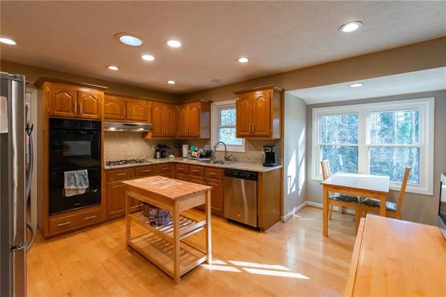 a kitchen with stainless steel appliances kitchen island granite countertop a refrigerator a stove top oven and a sink with island