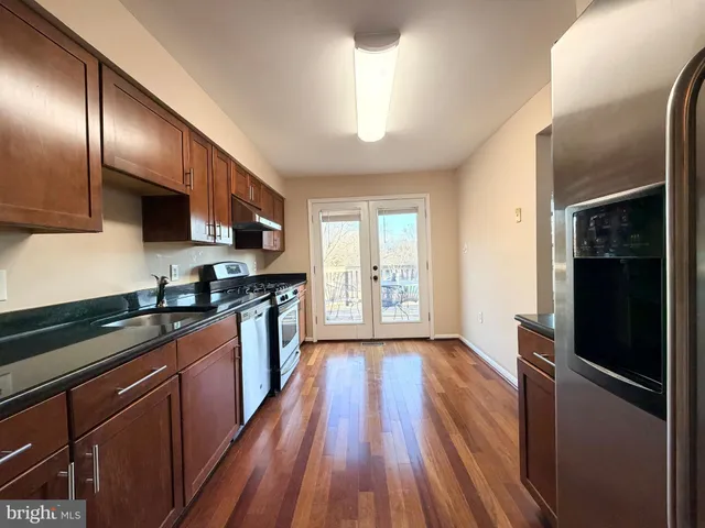 a kitchen with stainless steel appliances granite countertop a refrigerator a sink dishwasher a stove and white countertops with wooden floor