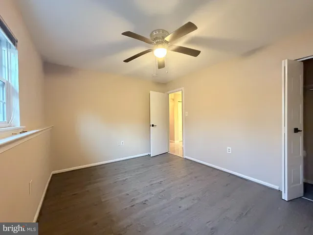 a view of an empty room with wooden floor and a ceiling fan