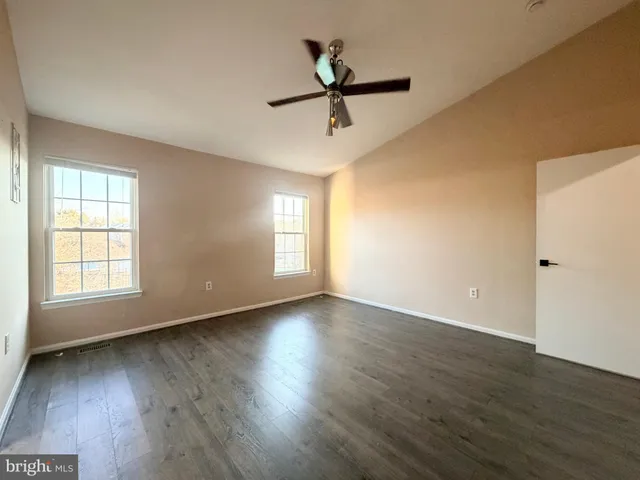 an empty room with wooden floor fan and windows