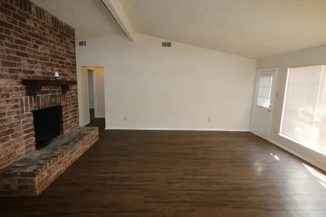 a view of an empty room with wooden floor fireplace and a window