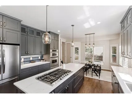 a kitchen with stainless steel appliances kitchen island granite countertop a refrigerator a stove and white cabinets with wooden floors