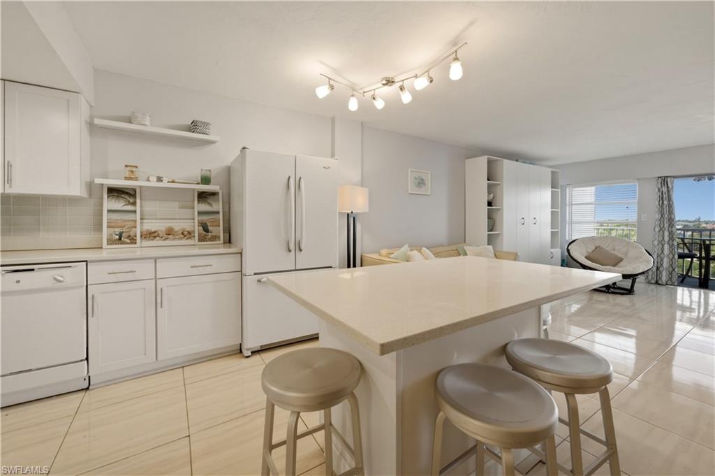 1 Bluebill Avenue, Unit 605 Naples, FL 34108 - Photo 14 of 20 Kitchen featuring open shelves, light countertops, white appliances, white cabinets, and a center island