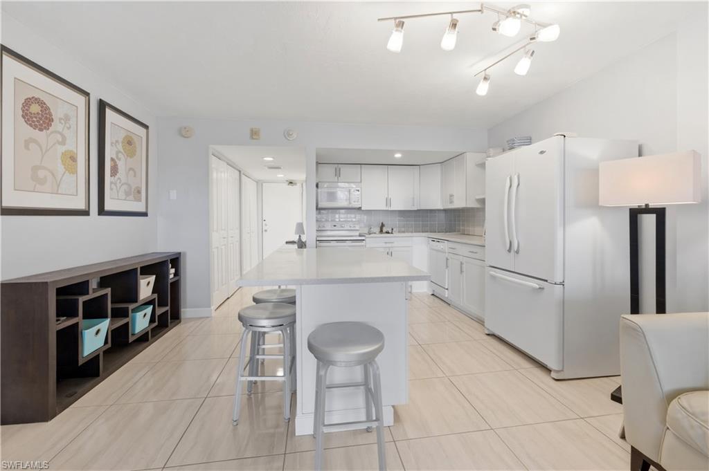 1 Bluebill Avenue, Unit 605 Naples, FL 34108 - Photo 16 of 20 Kitchen with white appliances, a kitchen breakfast bar, white cabinets, decorative backsplash, and a kitchen island