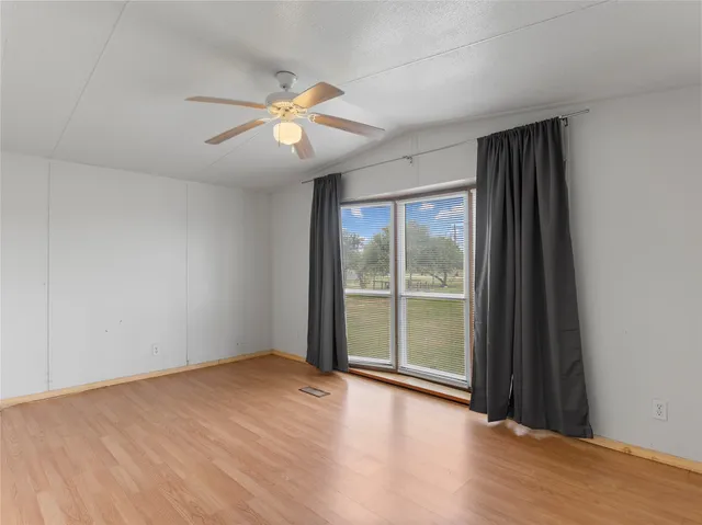 an empty room with wooden floor fan and windows