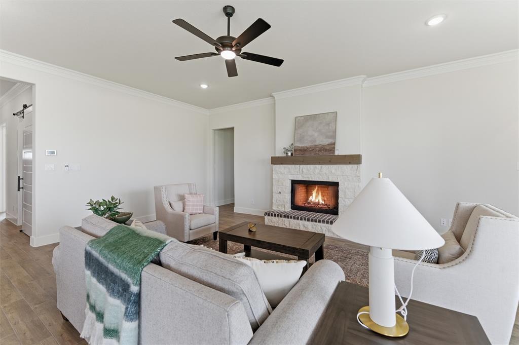 2433 Meteor Drive Krum, TX 76249 - Photo 16 of 29 Living area featuring a stone-clad fireplace with a wood mantel, wood-finish flooring, recessed lighting, crown molding, and a ceiling fan