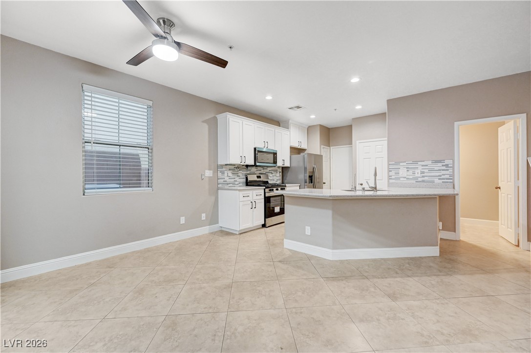 645 Monument Point Street Henderson, NV 89002 - Photo 11 of 54 Kitchen with white cabinetry, stainless steel appliances, backsplash, light tile patterned flooring, and ceiling fan