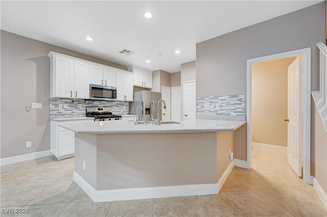645 Monument Point Street Henderson, NV 89002 - Photo 14 of 54 Kitchen with white cabinets, decorative backsplash, stainless steel appliances, light stone countertops, and a peninsula