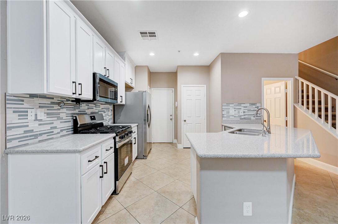 645 Monument Point Street Henderson, NV 89002 - Photo 15 of 54 Kitchen featuring stainless steel appliances, light tile patterned floors, decorative backsplash, light stone counters, and white cabinetry