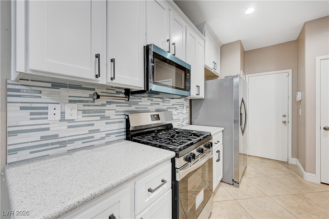 645 Monument Point Street Henderson, NV 89002 - Photo 16 of 54 Kitchen with appliances with stainless steel finishes, white cabinets, tasteful backsplash, light tile patterned floors, and light stone counters