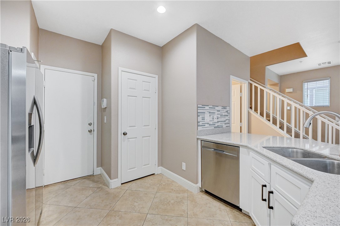 645 Monument Point Street Henderson, NV 89002 - Photo 18 of 54 Kitchen with decorative backsplash, appliances with stainless steel finishes, white cabinets, light stone counters, and light tile patterned flooring