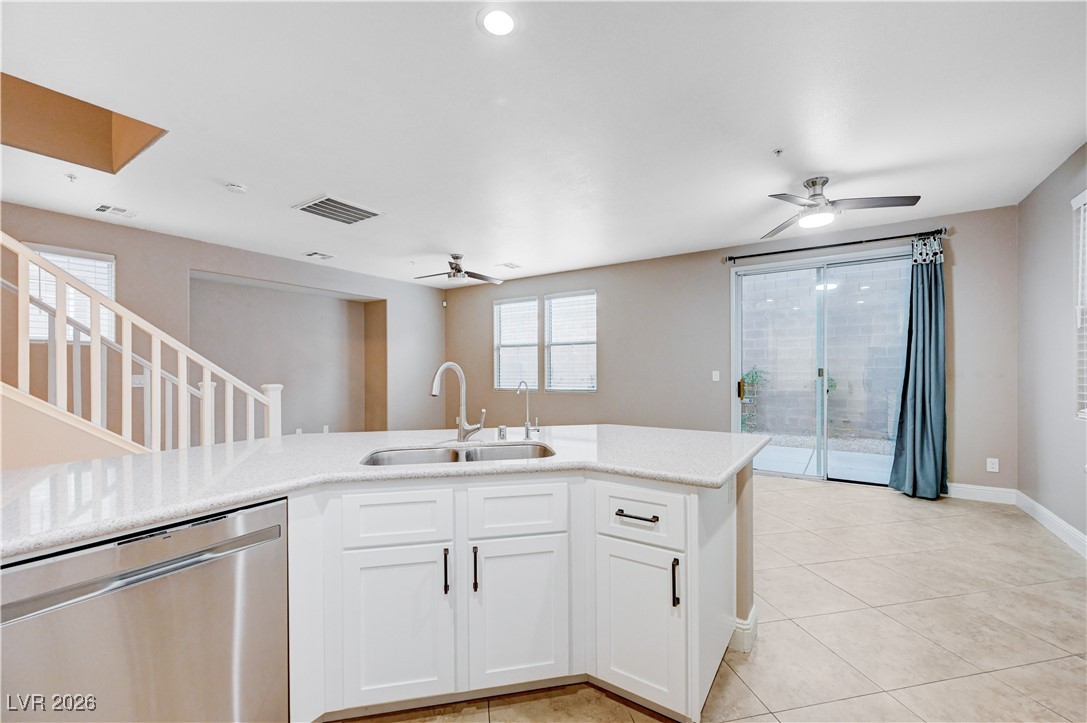 645 Monument Point Street Henderson, NV 89002 - Photo 19 of 54 Kitchen with stainless steel dishwasher, white cabinetry, a ceiling fan, light tile patterned flooring, and light stone counters