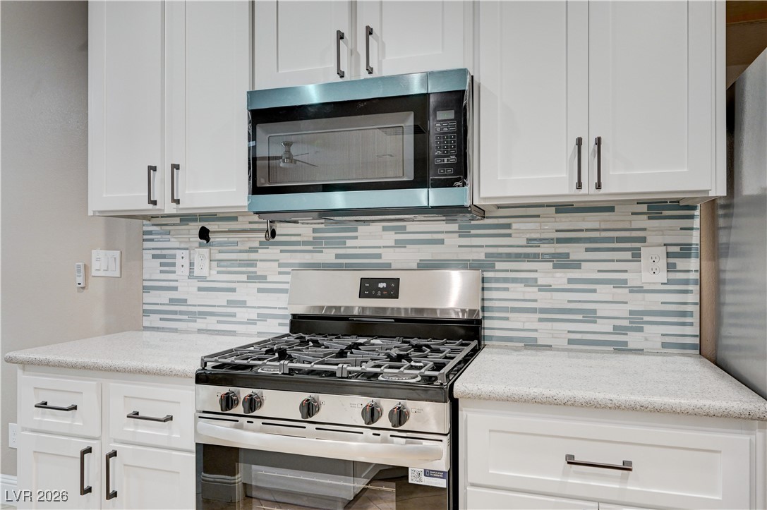 645 Monument Point Street Henderson, NV 89002 - Photo 22 of 54 Kitchen featuring stainless steel appliances, white cabinetry, and decorative backsplash
