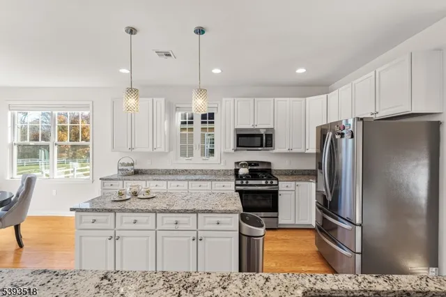 a kitchen with stainless steel appliances kitchen island granite countertop a refrigerator a sink a stove a dining table and chairs