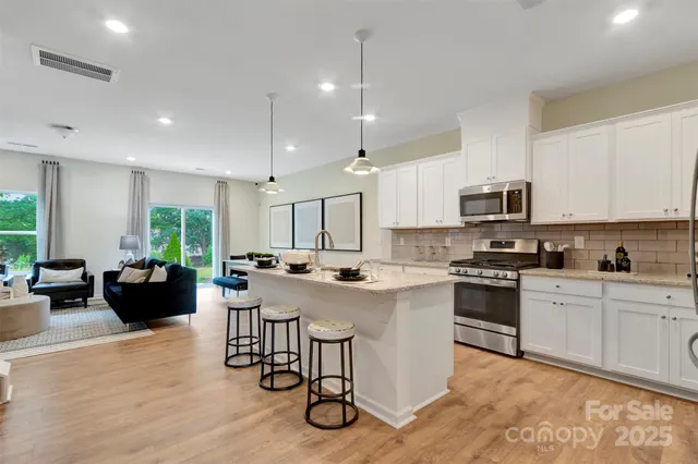 a kitchen with stainless steel appliances granite countertop a stove top oven a sink dishwasher a dining table and chairs with wooden floor