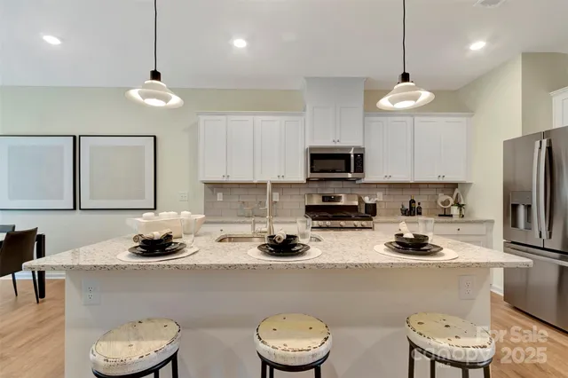 a kitchen with a white center island a oven a stove and a dining table with wooden floor