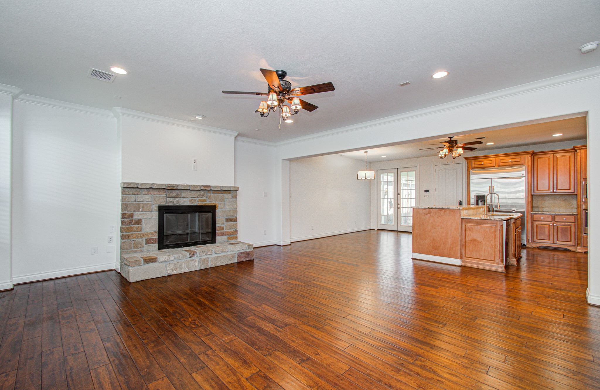 6621 North Main Street Houston, TX 77009 - Photo 7 of 41 This spacious living area features rich hardwood flooring, a cozy stone fireplace, and an open layout connecting to a modern kitchen with wooden cabinets and stainless steel appliances. French doors lead to the outdoor space, enhancing natural light.