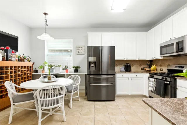 a kitchen with stainless steel appliances a dining table chairs stove refrigerator and cabinets
