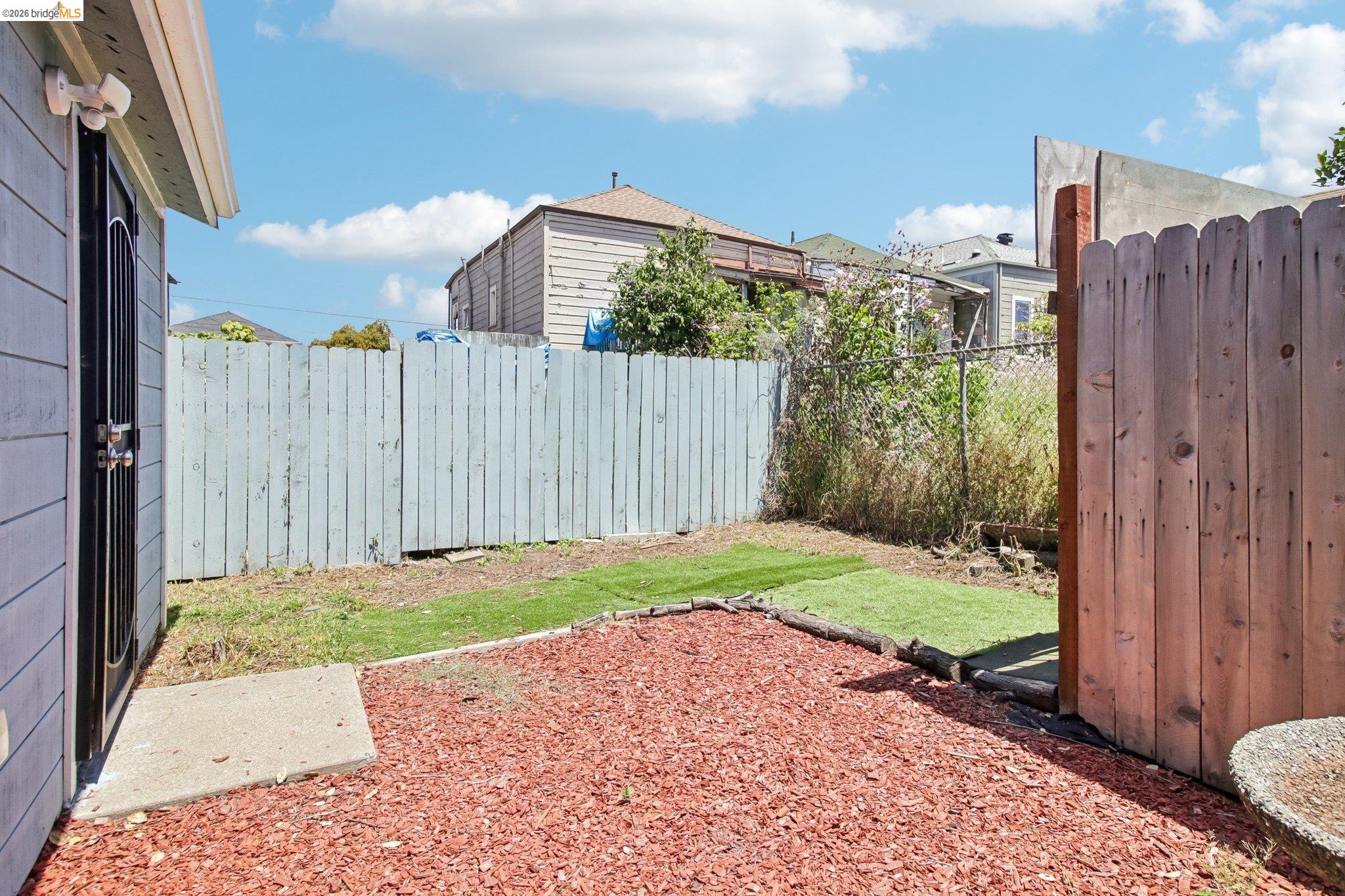 874 Pine Street Oakland, CA 94607 - Photo 25 of 39 Backyard area featuring red wood chip ground cover, a patch of artificial turf, and a concrete paver