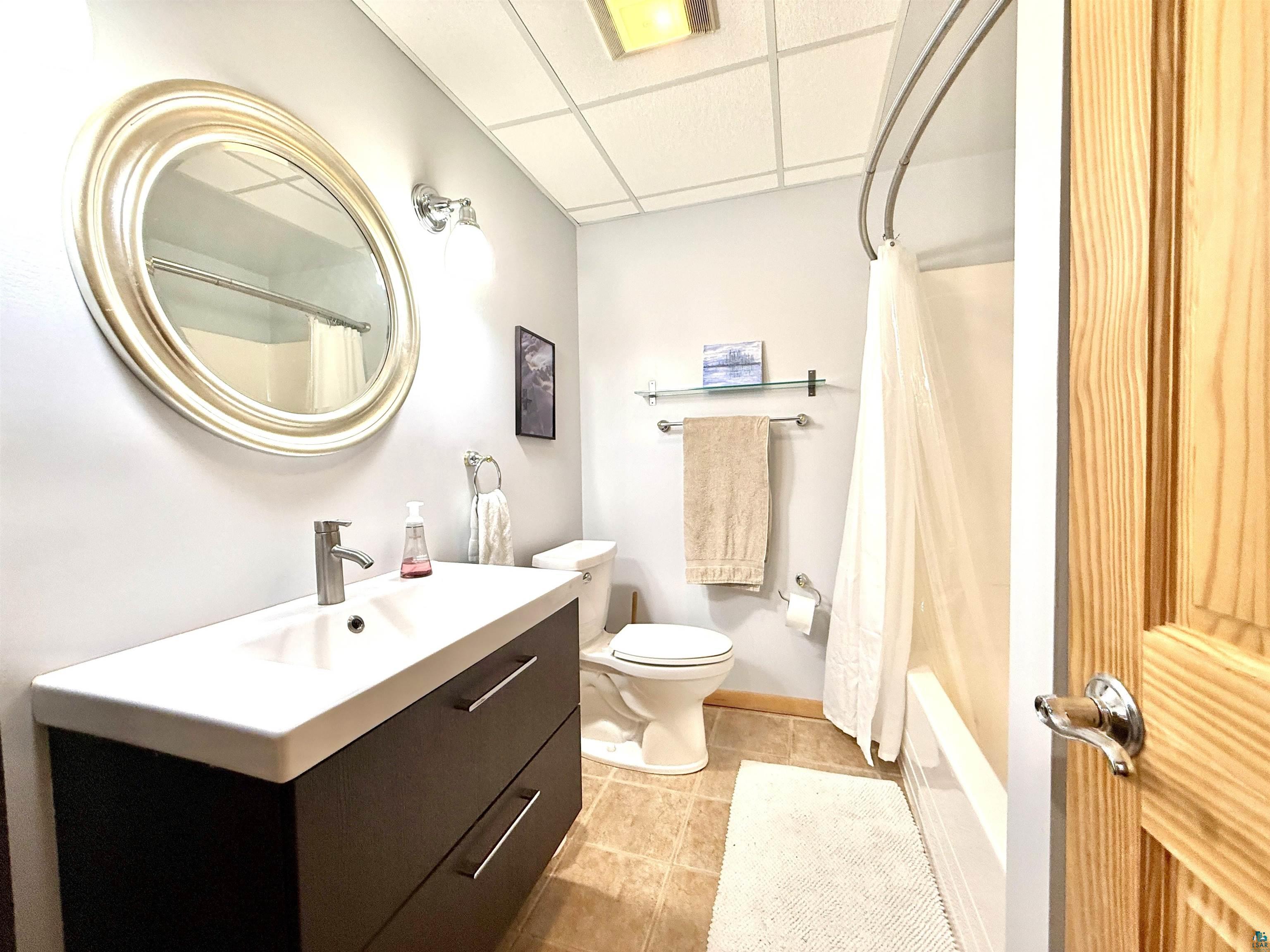 1787 North Bay Road Ely, MN 55731 - Photo 33 of 40 Bathroom featuring a dark wood-finish vanity with a white integrated sink, chrome faucet, and a large round mirror