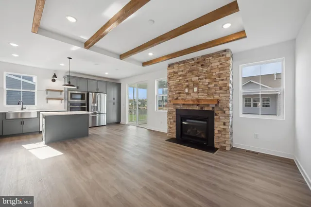 a living room with stainless steel appliances furniture a fireplace and a kitchen view