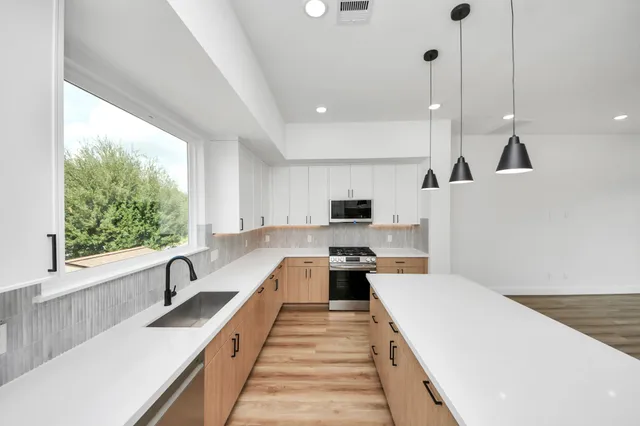 a large kitchen with kitchen island a large window a sink a counter space and stainless steel appliances