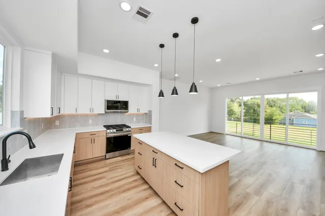 a large kitchen with stainless steel appliances granite countertop a large kitchen island a stove a sink a refrigerator and a granite counter tops with wooden floor