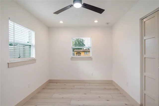 an empty room with wooden floor chandelier fan and windows