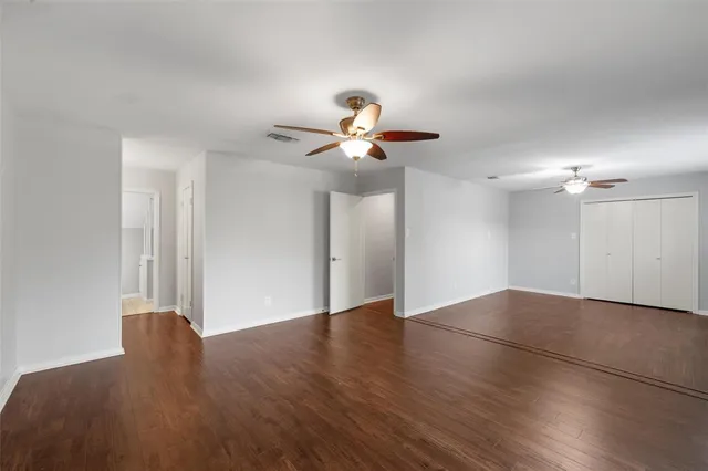 a view of an empty room with chandelier fan and wooden floor