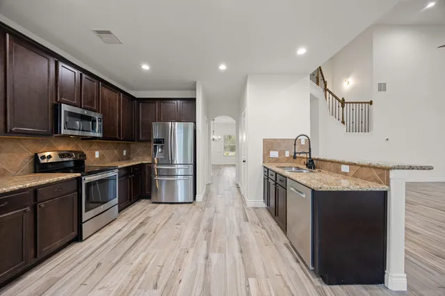 a large kitchen with stainless steel appliances granite countertop a stove a sink dishwasher and a refrigerator with wooden floor