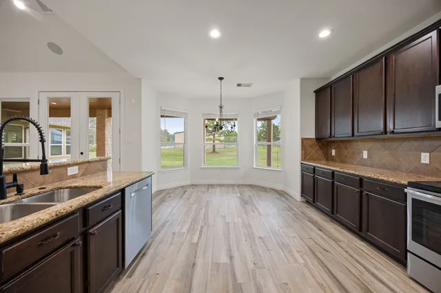 a kitchen with stainless steel appliances granite countertop wooden cabinets a sink a stove a refrigerator and microwave with wooden floor