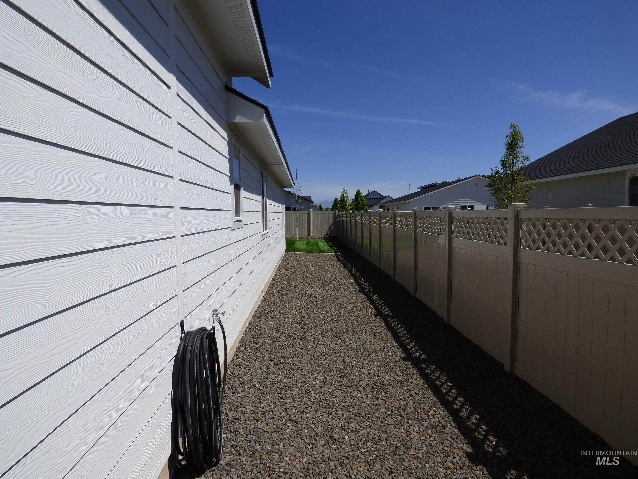 2708 East Buckaroo Drive Kuna, ID 83634 - Photo 44 of 48 Side exterior featuring white horizontal siding, a gravel pathway, and a tan privacy fence with lattice accents