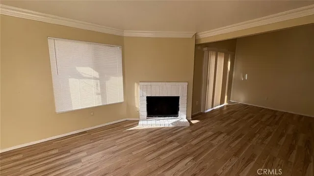 a view of an empty room with wooden floor fireplace and a window