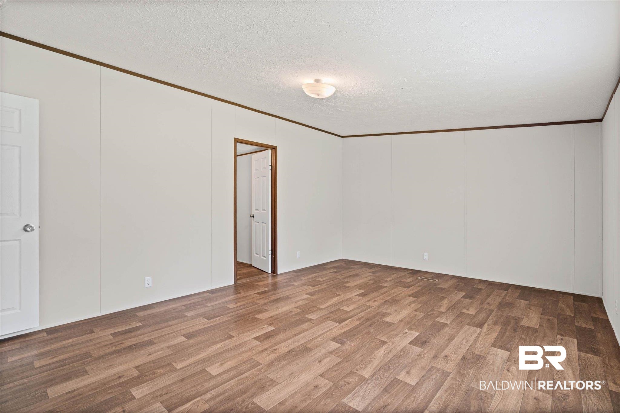 25366 Pollard Road Daphne, AL 36526 - Photo 12 of 22 Spacious room featuring wood-finish flooring, light-colored wall panels, and dark-toned trim