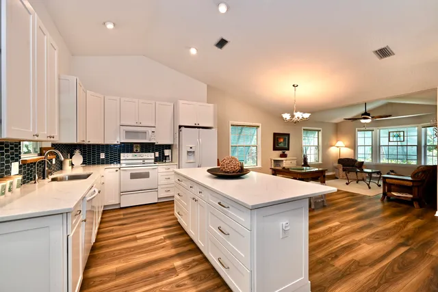 a large white kitchen with a stove top oven a sink a dining table and chairs with wooden floor