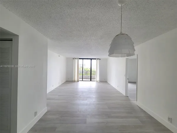 a view of an empty room with window and hardwood floor
