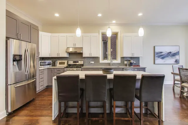 a kitchen with stainless steel appliances granite countertop a dining table chairs refrigerator and sink