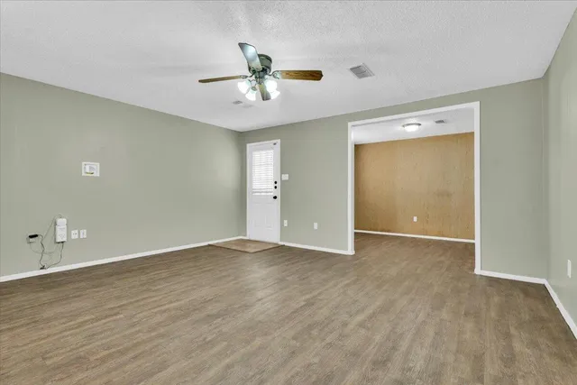 a view of an empty room with wooden floor and a ceiling fan