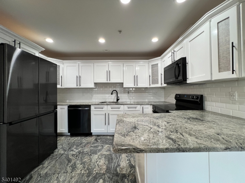 a kitchen with granite countertop a refrigerator sink and white cabinets