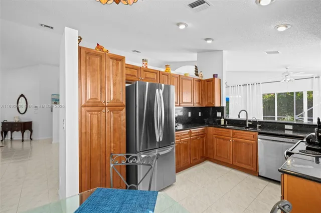 a kitchen with stainless steel appliances granite countertop a refrigerator a sink dishwasher a stove and a dining table with wooden cabinet