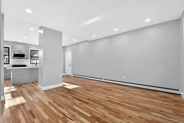 a view of an empty room with wooden floor and a kitchen