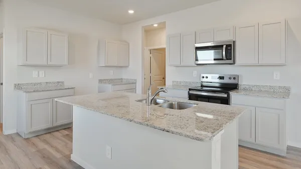 a kitchen with granite countertop a sink dishwasher stove and white cabinets with wooden floor