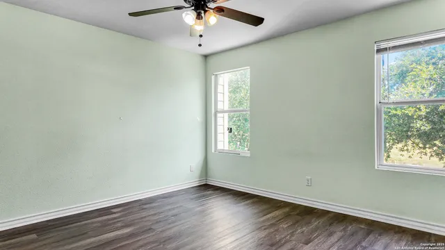 an empty room with wooden floor chandelier fan and windows