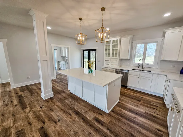 a large kitchen with kitchen island a stove a sink dishwasher a refrigerator white cabinets and wooden floor