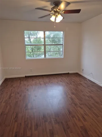 an empty room with wooden floor chandelier fan and windows