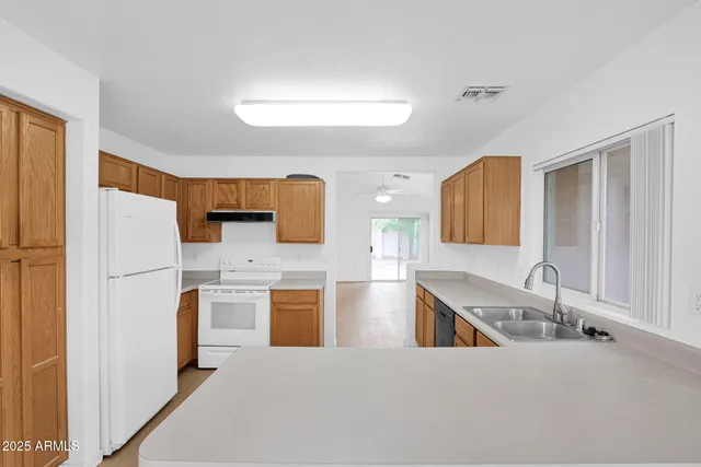 a kitchen with stainless steel appliances granite countertop a sink a stove top oven a refrigerator with white cabinets and wooden floor