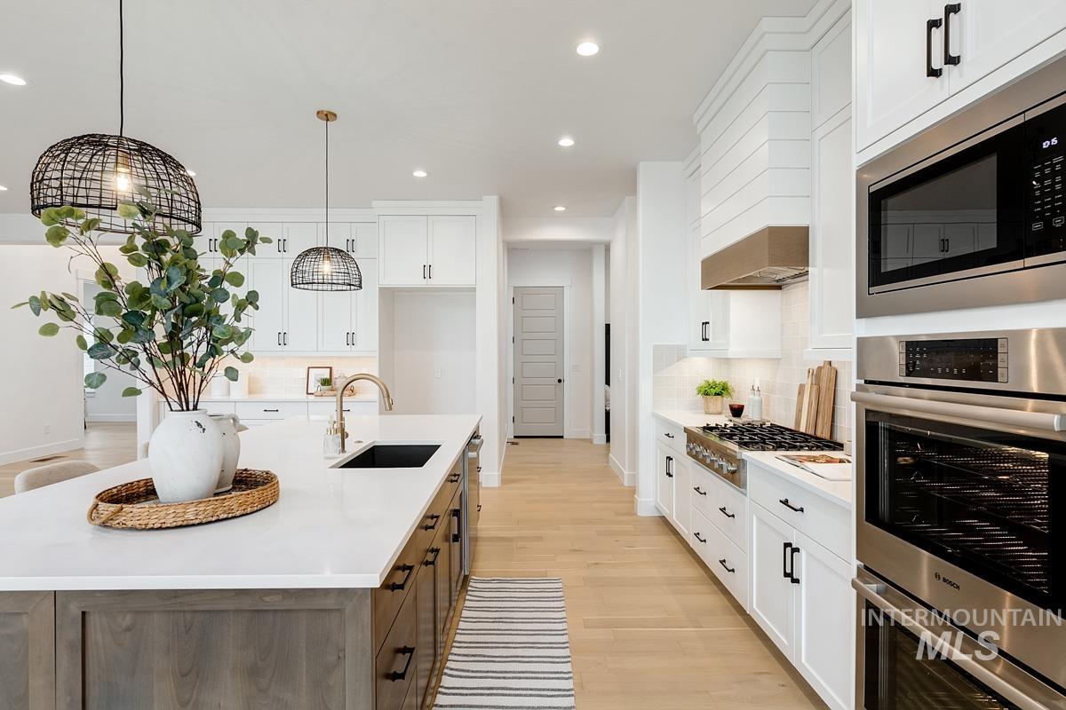 13624 North Ruffed Grouse Way Boise, ID 83714 - Photo 13 of 41 Kitchen with white cabinets, tasteful backsplash, appliances with stainless steel finishes, light wood-style floors, and an island with sink